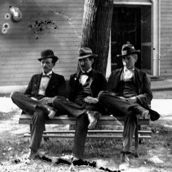 Black and white photo of three men sitting on a bench