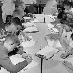 Black and white photo of children at desk cluster with heads bent over open books
