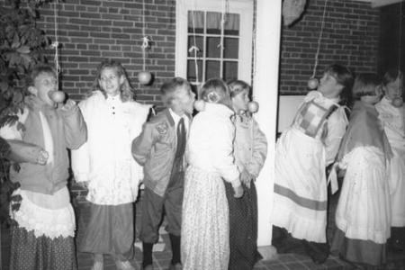 Children attempt to bite apples suspended from strings